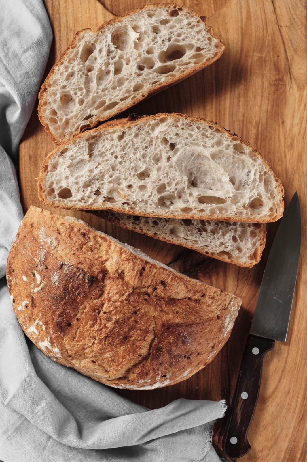 Sliced sourdough loaf showing an open, hole-filled crumb structure on a wooden cutting board with a knife.